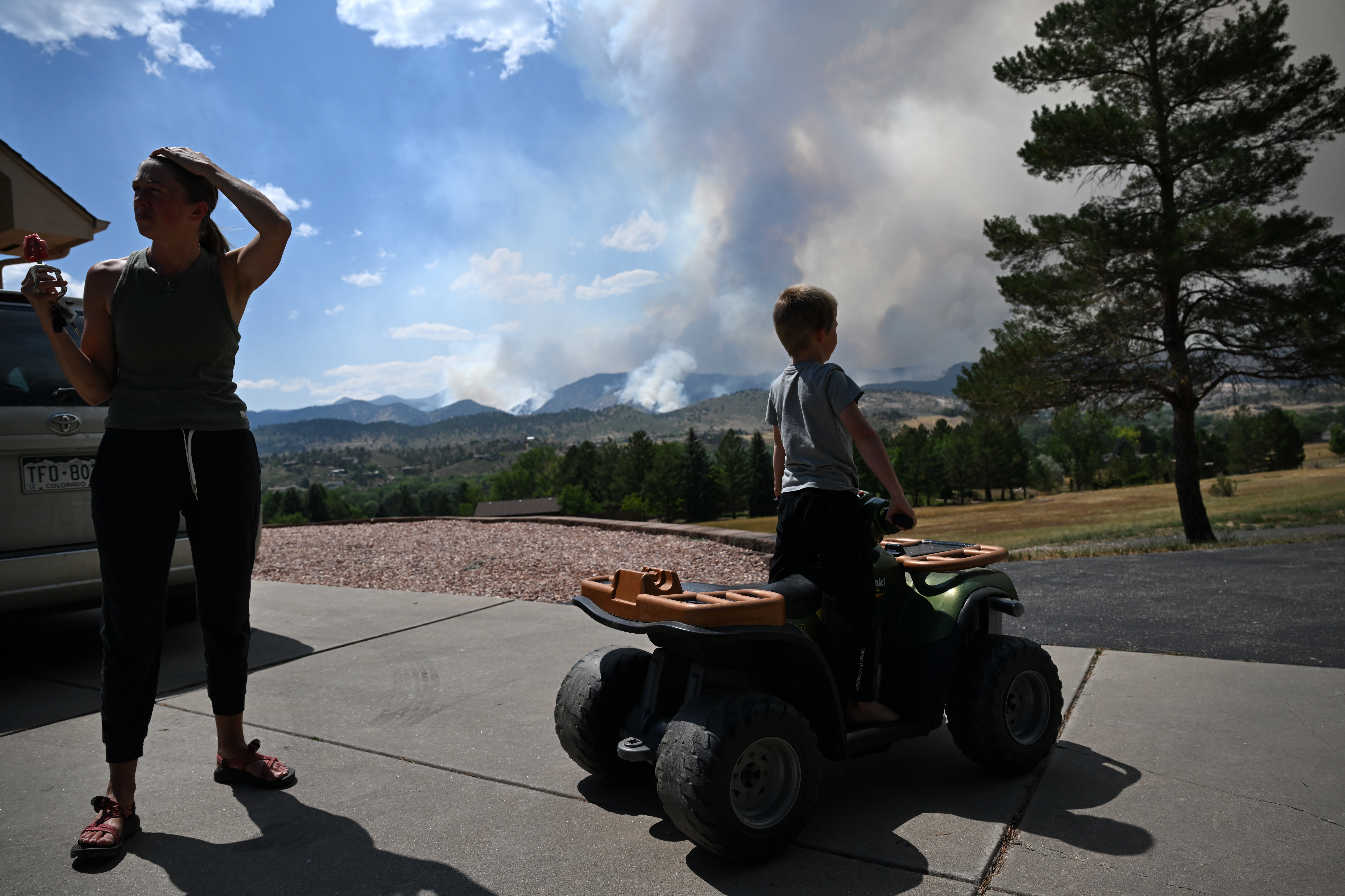 Deborah Mann, left, and her son, Basil Mann, 6, on his small ATV, try to stay cool eating popsicles at the home of Mann's parents while the Alexander Mountain fire continues to burn in the foothills west of their home off of Glade Road near Loveland on July 30, 2024. (Photo by Helen H. Richardson/The Denver Post)