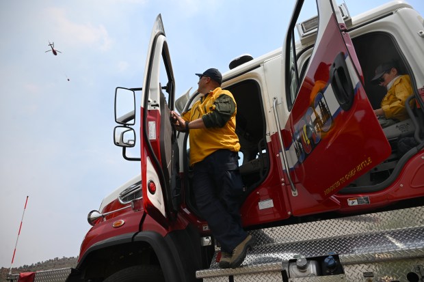 Stratmoor Hills Fire Protection engine boss John Ortiz, watches as helicopters pass by to drop water on the Alexander Mountain fire near Loveland on Wednesday, July 31, 2024. The engine was providing structure protection on the fire. At right is Hygiene Fire Protection District firefighter Jen Sampson. (Photo by Helen H. Richardson/The Denver Post)