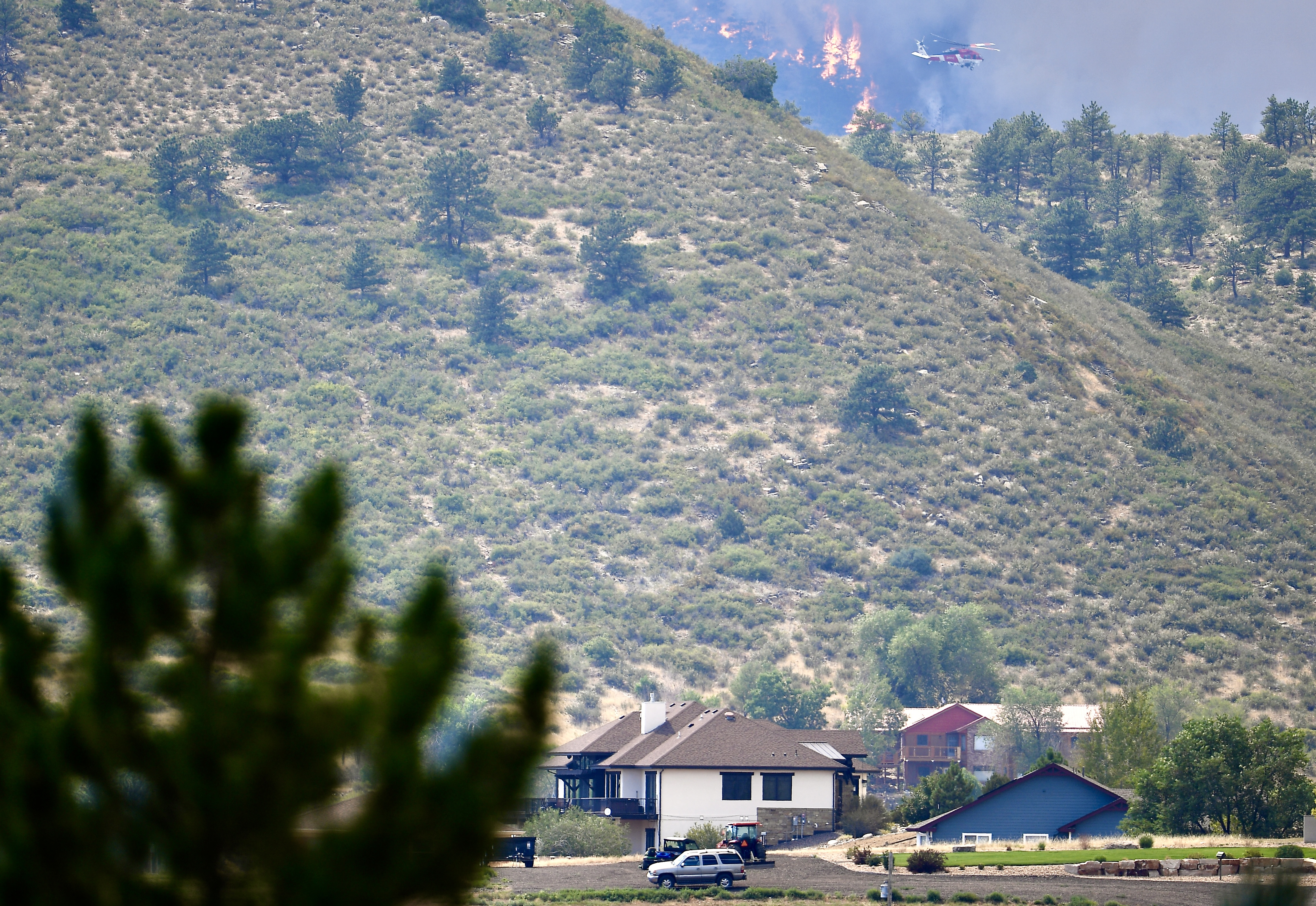 Flames can be seen as a helicopter passes over the Alexander Mountain fire near homes west of Loveland on Tuesday, July 30, 2024. (Photo by Zachary Spindler-Krage/The Denver Post)