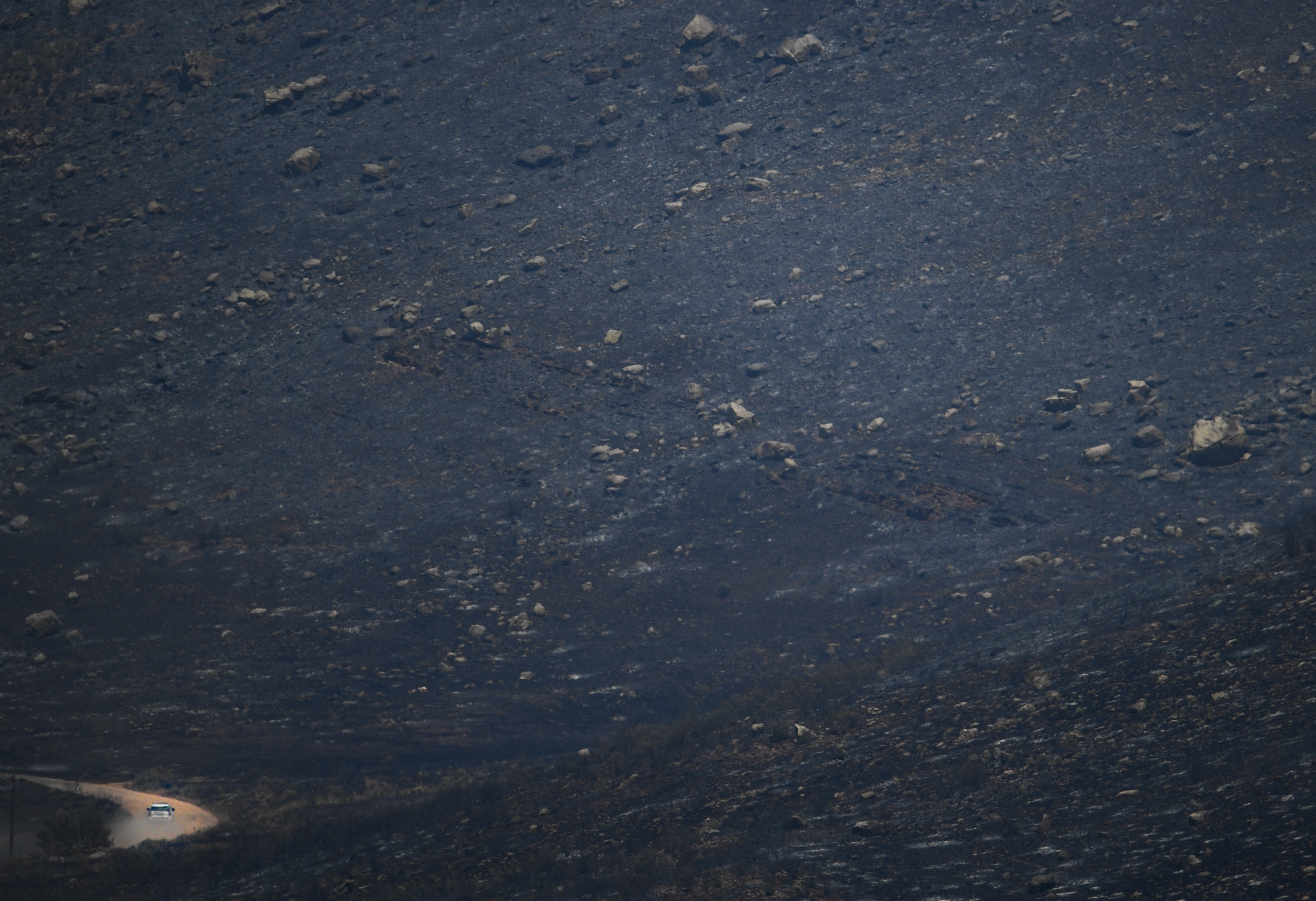 A police car, bottom left, drives through a desolate black landscape burned by the Stone Canyon fire near Lyons on Thursday, Aug. 1, 2024. (Photo by Zachary Spindler-Krage/The Denver Post)