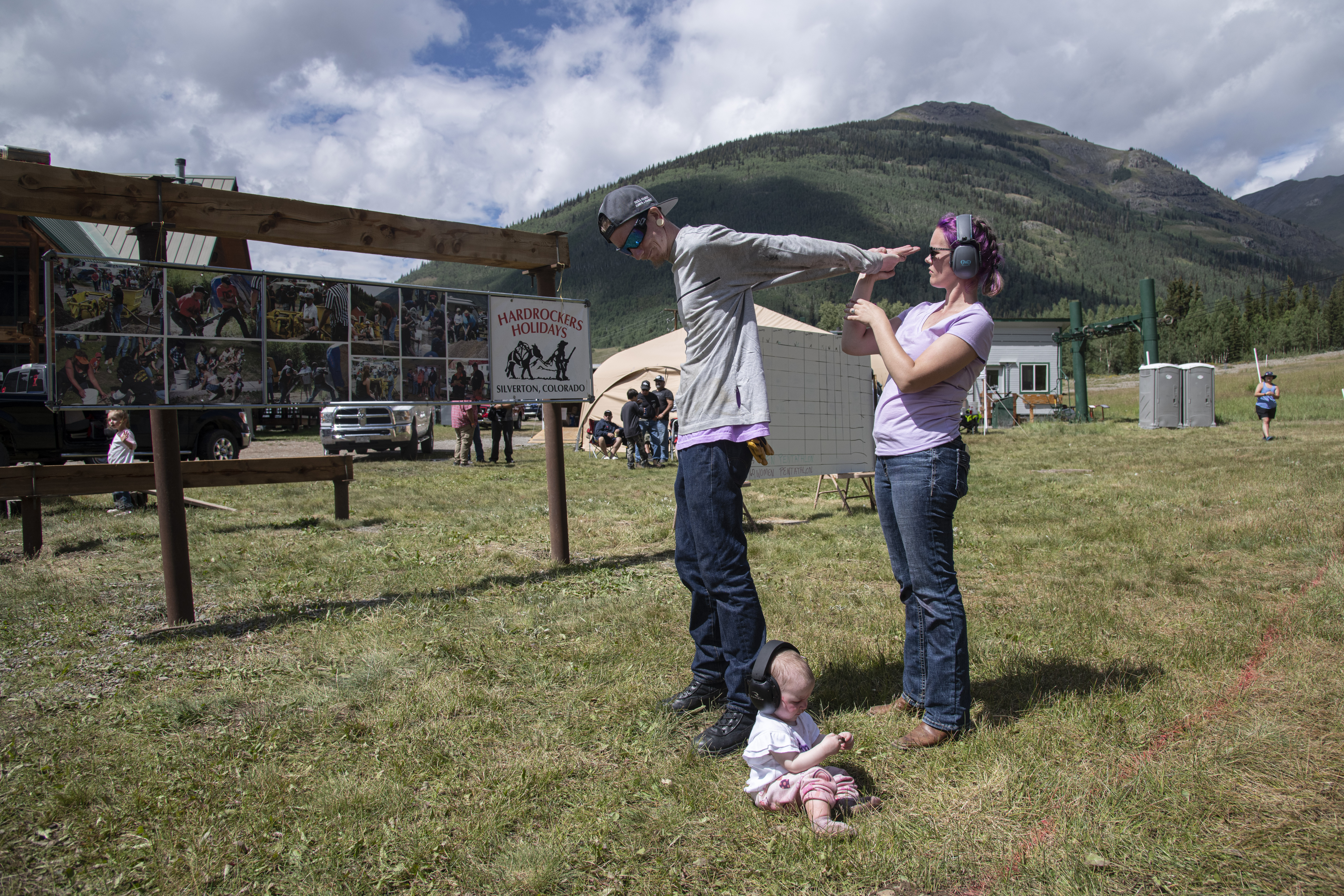 David Robinson has his arms stretched by his wife Morgan Robinson while their one-year-old daughter Emberly plays in the grass during drilling competition at the 50th Hardrockers' Holidays in Silverton on Saturday, Aug. 10, 2024. (Photo by William Woody/Special to The Denver Post)