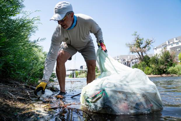 Dan Beyers picks up trash from the banks of the South Platte River near Commons Park on Saturday, July 20, 2024, in Denver. Beyers is an avid kayaker who frequently uses the South Platte River for recreation. Can'd Aid is a local non-profit that gathered volunteers and organized the Commons Park trash pickup. (Rebecca Slezak/Special to The Denver Post)